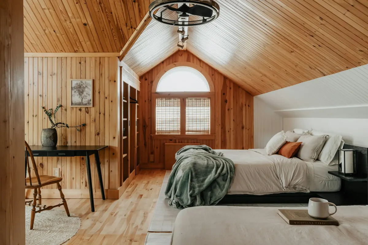 Dormitorio abuhardillado de madera con cama, manta verde y una taza de café